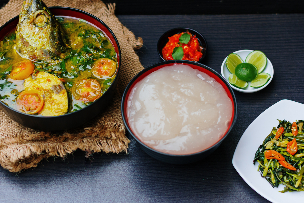 Foto pemandangan meja makan yang diatur dengan papeda dan berbagai lauk pauk seperti ikan bakar dan sayuran, memberikan gambaran tentang bagaimana papeda biasanya disajikan dalam acara keluarga di Maluku